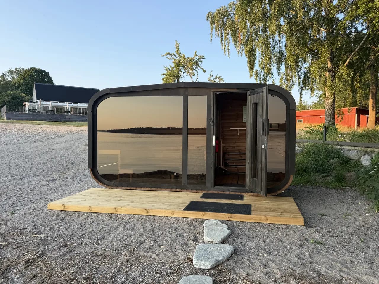 Sjöbastun på sandstranden vid Kaggeholm i kvällssol, med öppen dörr och Mälaren speglad i glasfronten
