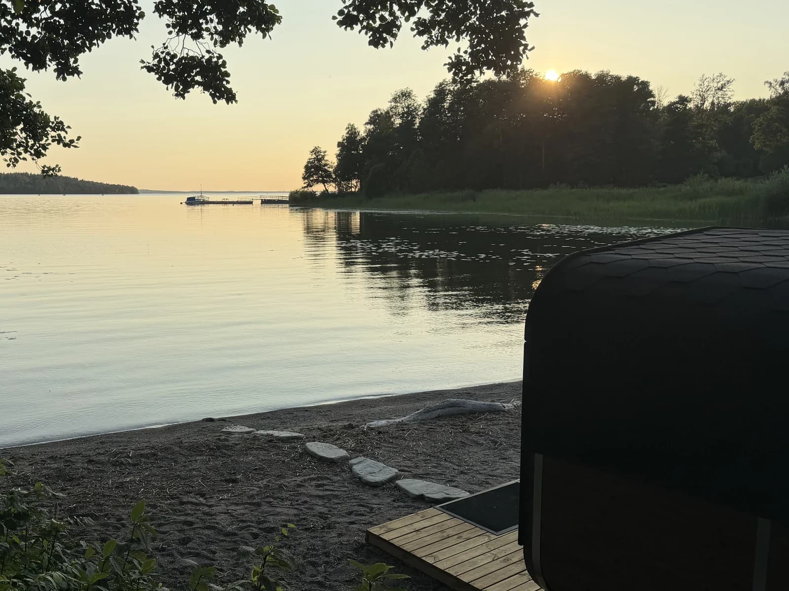 Solnedgång över Mälaren vid stranden på Kaggeholm, med bastun och trädäcket på sanden