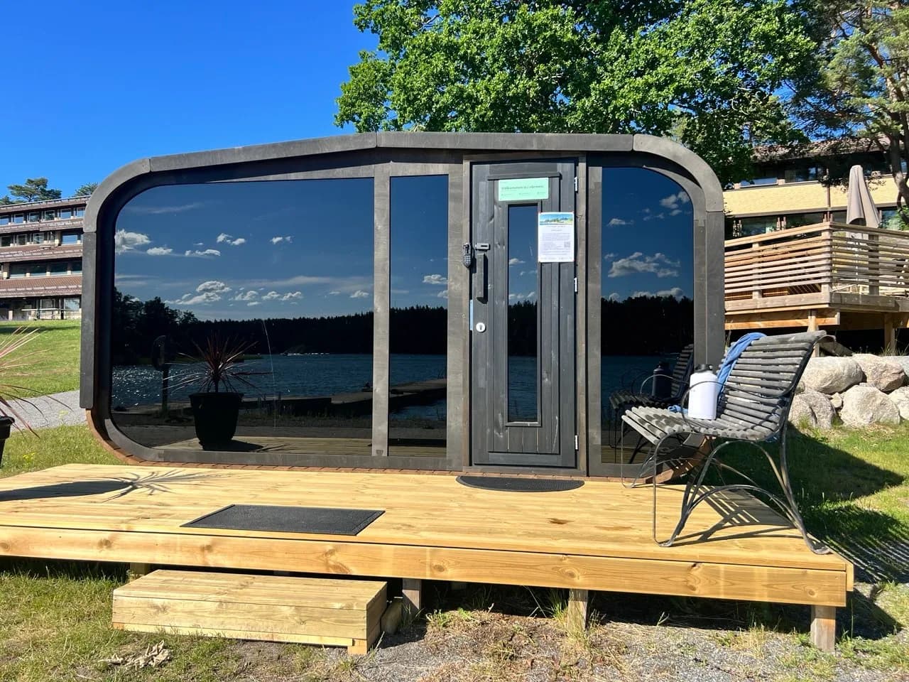Saunify bastu i Åkersberga framifrån med stor glasfront som speglar skärgården, trädäck och sittplats i kvällssol
