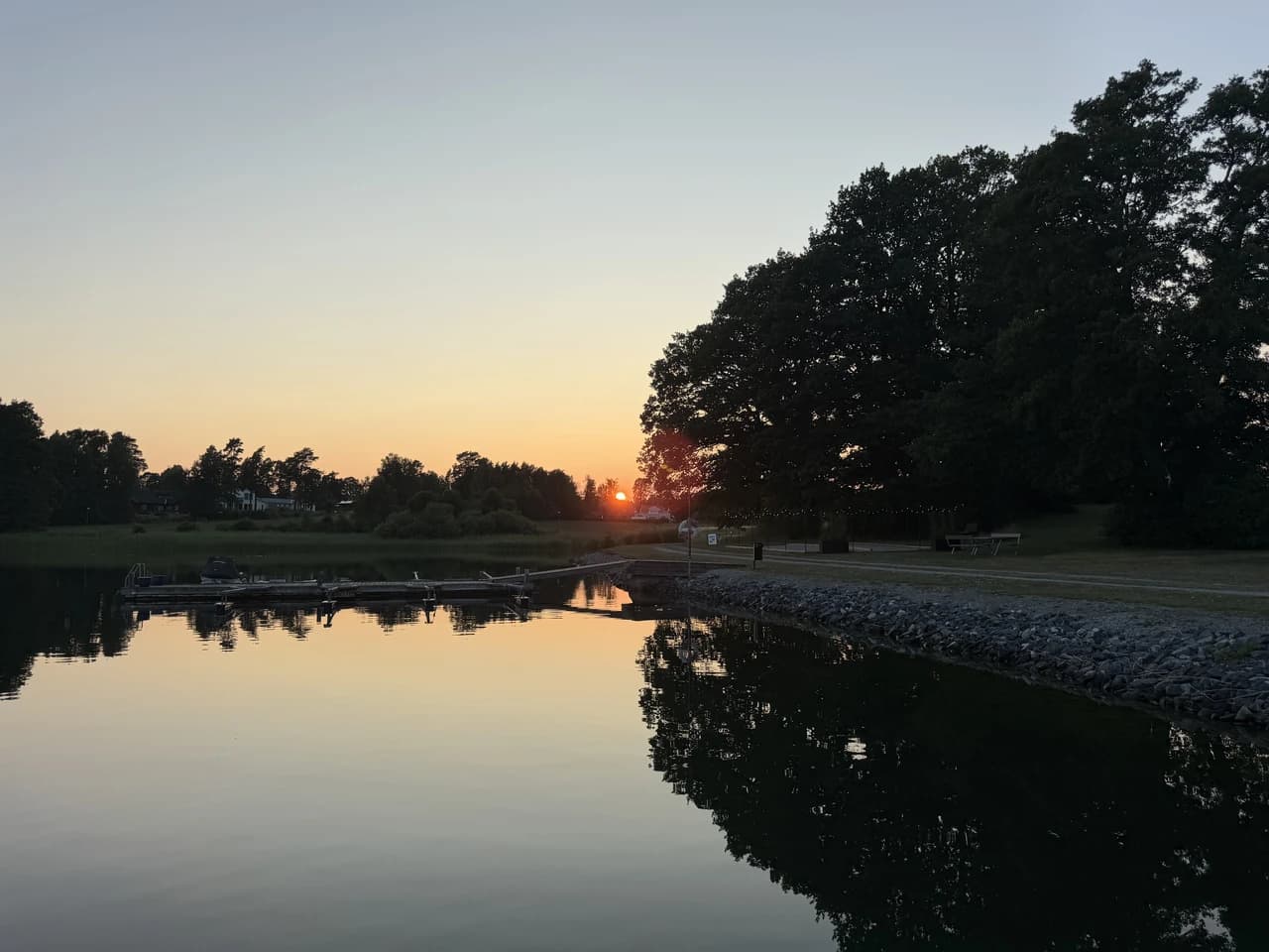 Solnedgång över skärgårdsviken vid Skåvsjöholm, med bryggorna speglade i det stilla vattnet